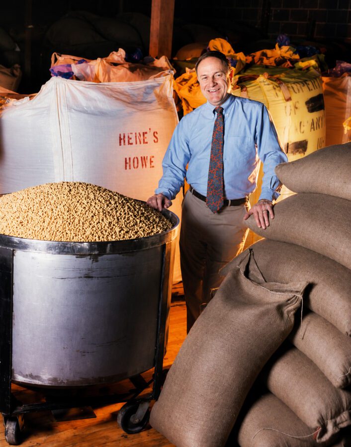 president of a company standing in his warehouse, surrounded by some of his products, in this case, roasted nuts.